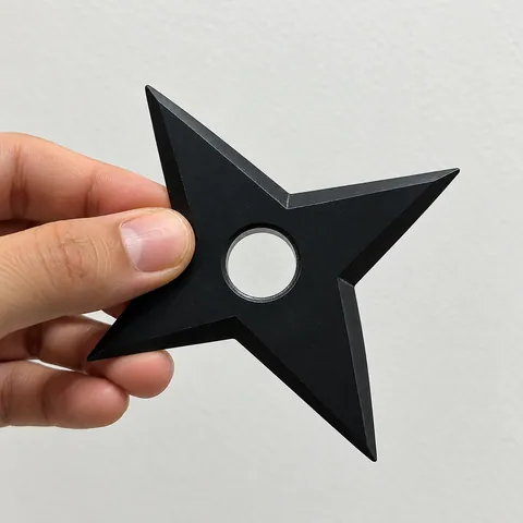 Mão segurando uma shuriken decorativa preta, mostrando a escala e a textura da peça impressa em 3D.